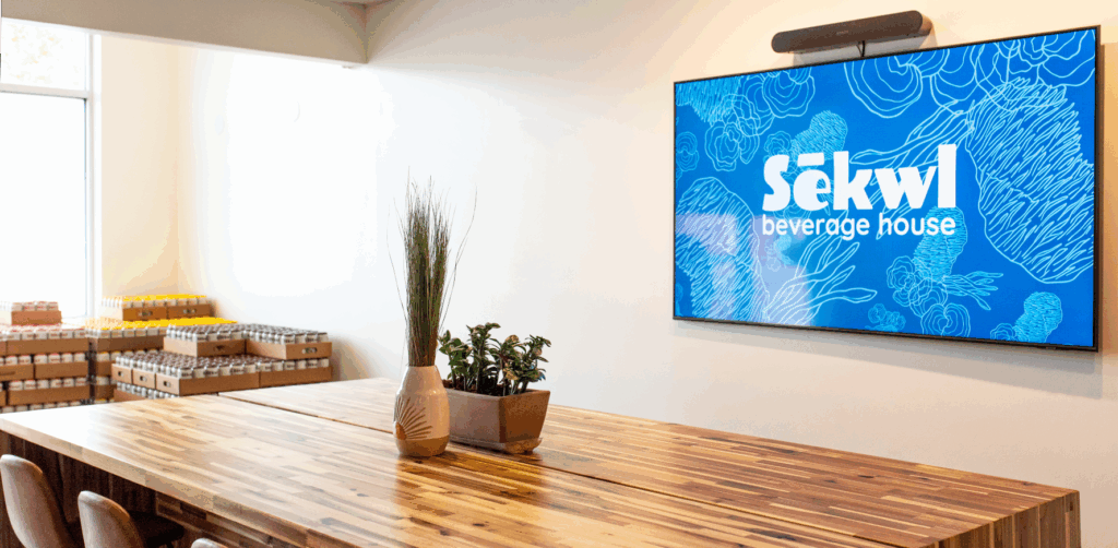 A brightly lit room with a wood table and a screen with the Sekwl logo in the background