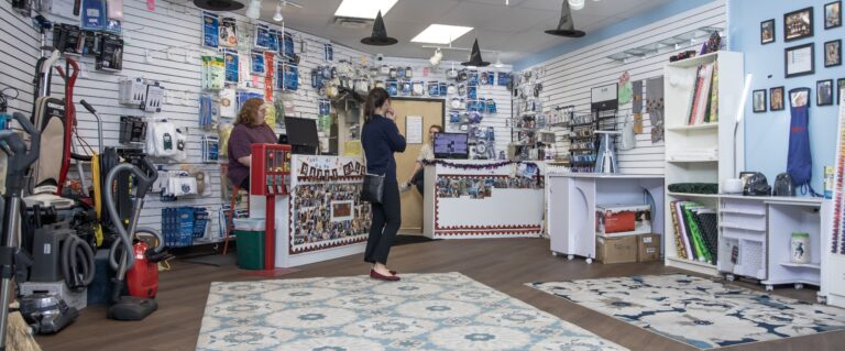 Bright showroom with rugs on the floor and people standing around a desk next to thread.