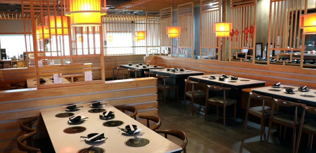 Warmly lit brown wood restaurant interior with black dishes set on table tops with personal stoves