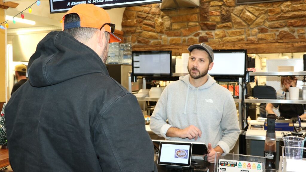 Man standing at a cash register taking a man's order at a warmly lit restaurant