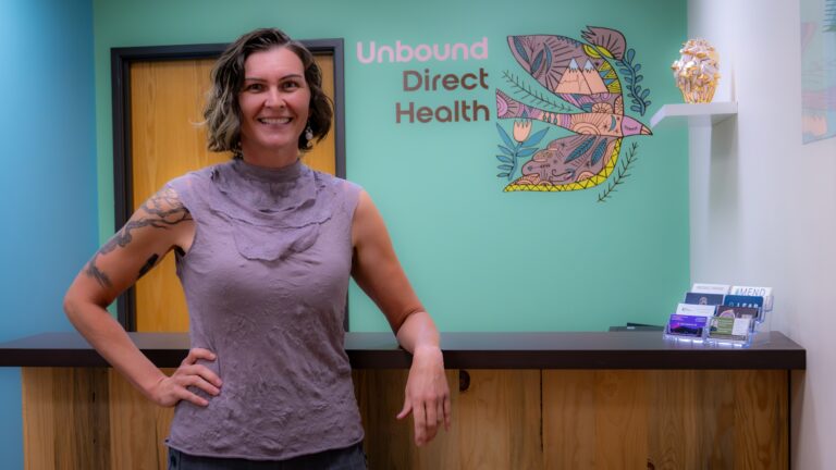 Doctor smiling in a medical office with Unbound Direct Health logo