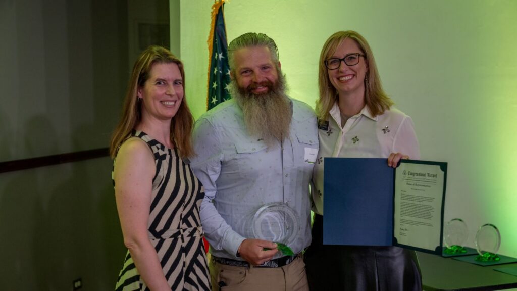 Three people smiling with an award